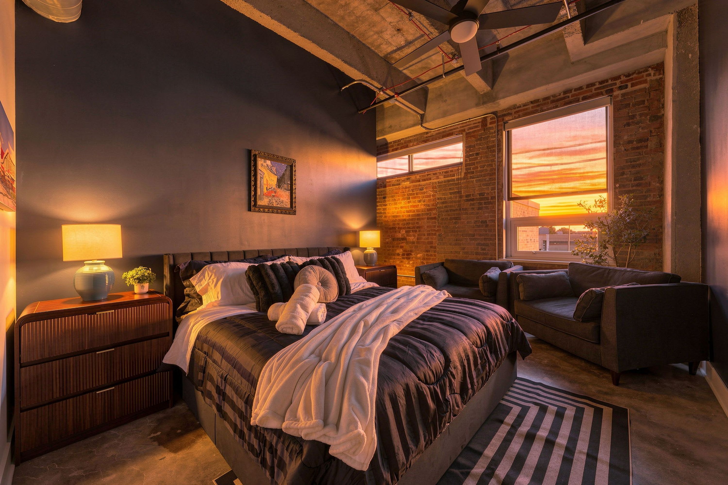 Un dormitorio moderno con una cama grande, un sofá, un escritorio y una ventana con vistas al atardecer.