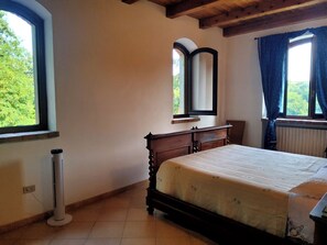 A bedroom with a bed, a standing heater, a window with curtains, and a mirror on the wall. - Privacy, tranquility, relaxation, nature, culture, and traditions. Pet-friendly (Piemonte)