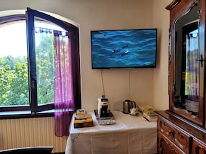 A room with a television mounted on the wall displaying a sea scene, a table with a white tablecloth, a coffee maker, and a cabinet with a mirror. - Privacy, tranquility, relaxation, nature, culture, and traditions. Pet-friendly (Piemonte)