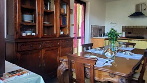 A dining area with a wooden table set for four, surrounded by chairs. A large wooden cabinet with glass doors is to the left.