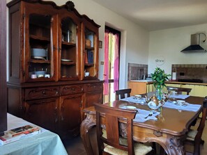 A dining area with a wooden table set for four, surrounded by chairs. A large wooden cabinet with glass doors is to the left.