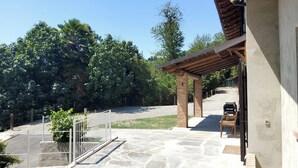 A stone patio with a wooden pergola, a fenced area, and a gravel path leading to a building.