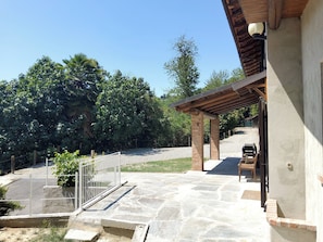 A stone patio with a wooden pergola, a fenced area, and a gravel path leading to a building.