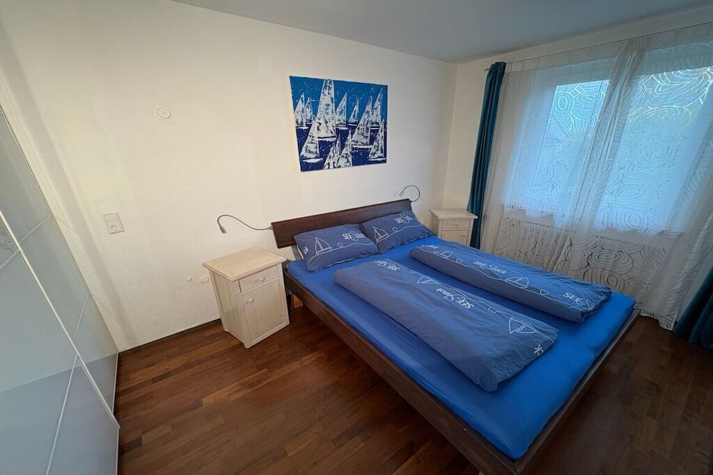 Ein Schlafzimmer mit einem Bett, einem Nachttisch, einem Wandbild und einem Fenster mit Vorhängen.