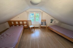 Un dormitorio ático pequeño y triangular con dos camas individuales, una silla de madera y una mesita.