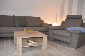 A living room with a grey sofa, a wooden coffee table, and a small side table with a book. - Holiday apartment with 2 bedrooms (Timmendorfer Strand)
