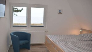 Ein Schlafzimmer mit Bett, einem Sessel, einem Fenster mit Meerblick und einer Wandleuchte.