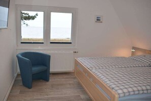 Een slaapkamer met een bed, een stoel, een raam met uitzicht op zee en een wandlamp.