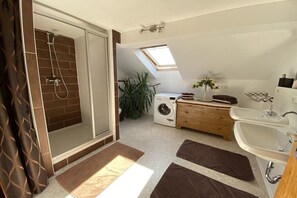 Un bagno moderno con doccia, lavatrice, lavandino e finestra a lucernario.