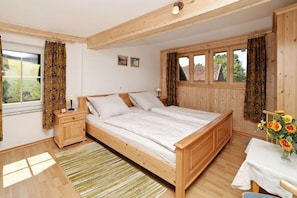Una camera da letto con un letto in legno, un comodino, una finestra con tende e un tavolino con un vaso di fiori.