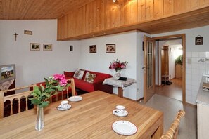 A wooden dining table with plates and a vase of flowers, a red sofa, and a wooden ceiling. - Brotjacklriegel - Pletl-Hof (Schönberg)