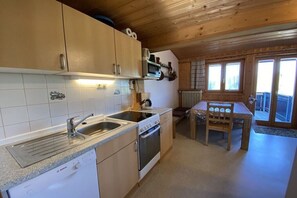 A kitchen with a Bosch dishwasher, stove, and sink, wooden cabinets, and a dining table with chairs. - Brotjacklriegel - Pletl-Hof (Schönberg)