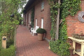 Un bâtiment en briques avec un chemin également en briques menant à un banc blanc et à une table sur laquelle est posée une plante en pot.