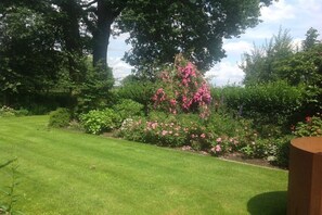 Un jardin bien entretenu, agrémenté de diverses plantes à fleurs et d’un grand arbre qui offre de l’ombre.