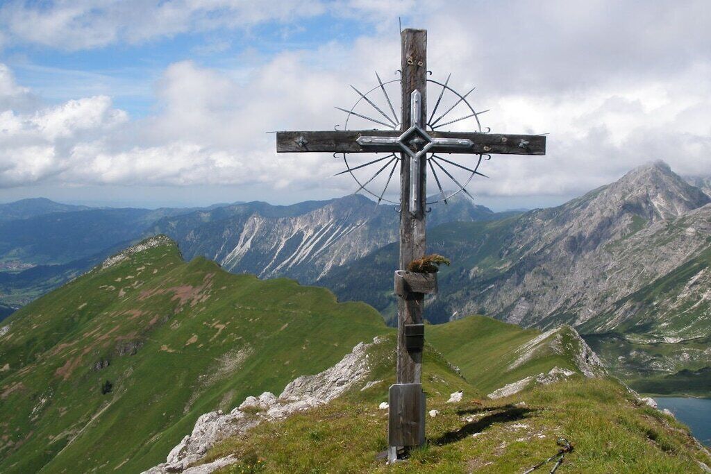 Uma cruz de madeira com design de bússola, ao fundo montanhas.