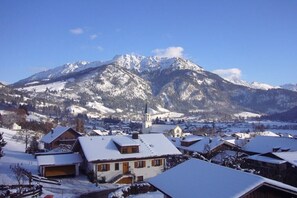 Ein verschneites Dorf mit traditionellen Häusern und einer Kirche, umgeben von Bergen.