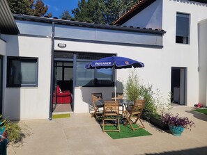 Eine Terrasse mit Tisch, Stühlen, einem blauen Sonnenschirm und einem roten Stuhl.