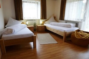Une chambre avec deux lits simples, un plancher en bois, une table de chevet avec une lampe et une fenêtre avec des rideaux.