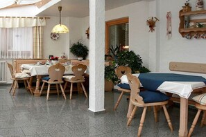 Un coin repas avec des chaises et des tables en bois, une plante en pot et un banc agrémenté d’un coussin bleu.