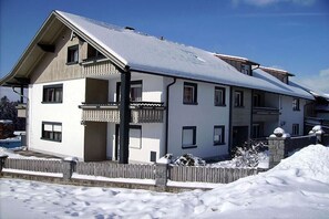 Ein zweistöckiges Gebäude mit Balkon, Garage und einem mit Schnee bedeckten Dach.