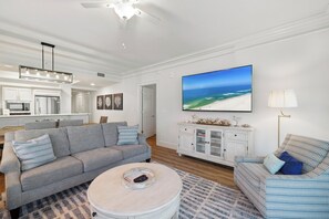 Ein modernes Wohnzimmer mit einem grauen Sofa, einem Couchtisch und einem Fernseher, der eine Strandansicht zeigt.