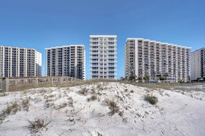 Un hôtel en bord de mer, composé de plusieurs immeubles de grande hauteur, avec une plage de sable au premier plan et un ciel bleu dégagé.