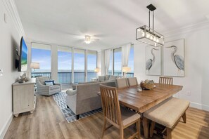 Un vaste espace de vie comprenant une grande table à manger en bois, des sièges confortables et une vue sur l’océan grâce à de grandes fenêtres.