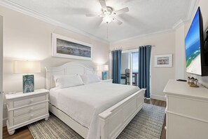 Une chambre à coucher avec un lit, des tables de chevet, un ventilateur de plafond, un tableau, une télévision et une vue sur l’océan.