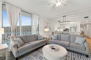 Ein modernes Wohnzimmer mit grauen Sofas, einem runden Couchtisch und Blick auf einen Pool und Gebäude.