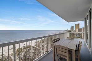 Un balcon avec vue sur la plage et l’océan, une table et des chaises, ainsi qu’une balustrade.