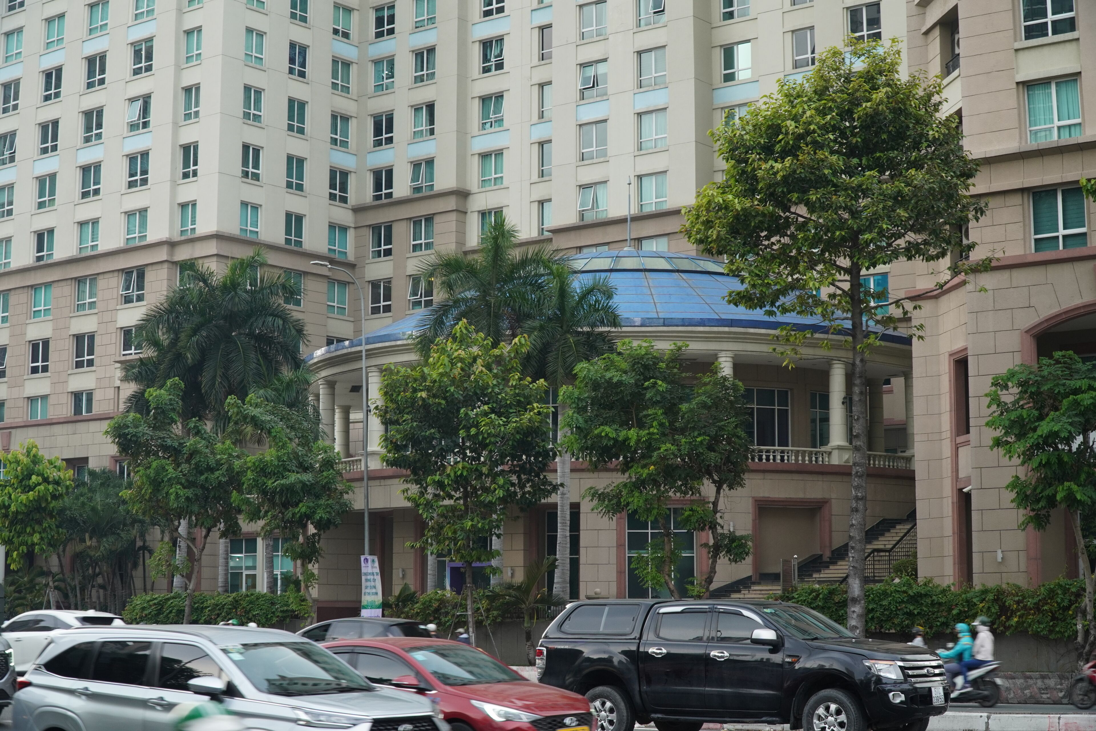 A multi-story building with a central atrium, surrounded by parked cars and trees.