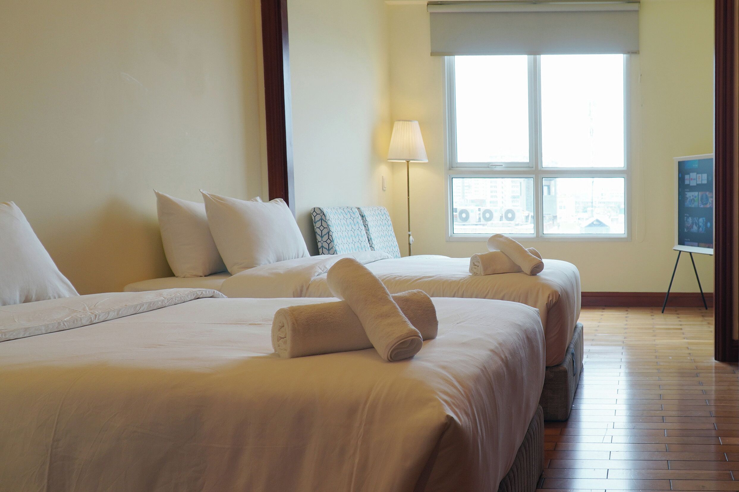A hotel room with two beds, a window, a lamp, and a view of the city.