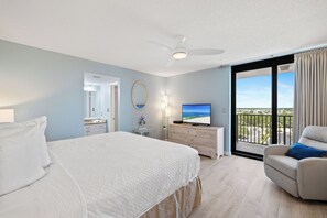 Et hotelværelse med seng, tv, skrivebord, stol og balkon med udsigt.
