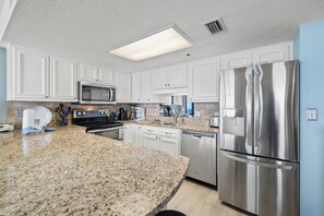 A modern kitchen with white cabinetry, stainless steel appliances, granite countertops, and a built-in microwave. - Phoenix East II 2091 by Liquid Life (Orange Beach)