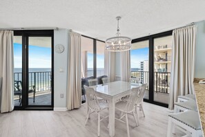 Spiseområde med et glasbord, stole, en lysekrone og havudsigt.