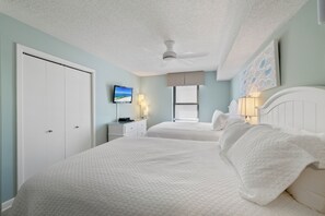 Een slaapkamer met twee bedden, een plafondventilator, een televisie en een raam met zonwering.