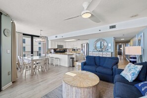 A spacious living area with a blue sofa, a dining table with chairs, a kitchen with white cabinets, and a ceiling fan. - Phoenix East II 2091 by Liquid Life (Orange Beach)