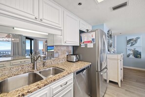 A modern kitchen with granite countertops, stainless steel appliances, and white cabinetry. - Phoenix East II 2091 by Liquid Life (Orange Beach)
