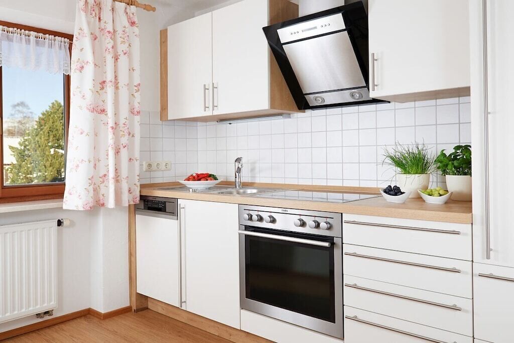 A modern kitchen with white cabinetry, a stainless steel range hood, and a dishwasher.
