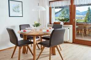 A dining area with a round table, four chairs, and a window with a view of mountains. - Type B | House Hornblick (Oberstdorf - Schöllang)