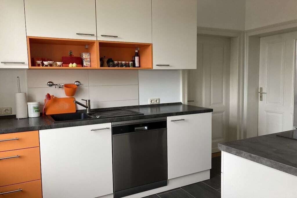 Une cuisine moderne avec des meubles blancs, un lave-vaisselle noir et une bouilloire orange.