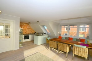 A modern kitchen with a brick accent wall, a dining area with wicker furniture, and large windows. - Knutt in the house Bill15 (Juist)