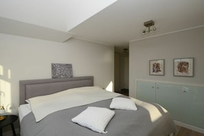 A bedroom with a bed, a nightstand, a wall-mounted light, and a door leading to another room. - Knutt in the house Bill15 (Juist)