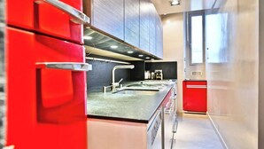 A modern kitchen with stainless steel appliances, a black countertop, and red cabinetry. - AN EXCELLENT COMBINATION OF PARISIAN CHARM & CENTRAL CONVENIENCE - SAINT GERMAIN (Paris)