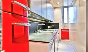 Una cocina moderna con electrodomésticos de acero inoxidable, una encimera negra y armarios rojos.