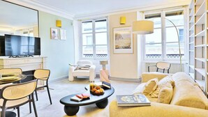 A modern living room with a sofa, chairs, a coffee table, a TV, and a bookshelf. - AN EXCELLENT COMBINATION OF PARISIAN CHARM & CENTRAL CONVENIENCE - SAINT GERMAIN (Paris)