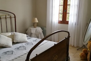Ein Schlafzimmer mit einem Bett, einem Nachttisch mit Lampe, einem Fenster mit Vorhängen und einem Teddybären auf dem Boden.