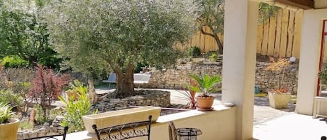 Un patio al aire libre con una mesa y sillas, rodeado de plantas en macetas y un muro de piedra.