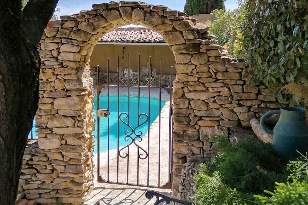 A stone archway leading to a pool area with a metal gate.