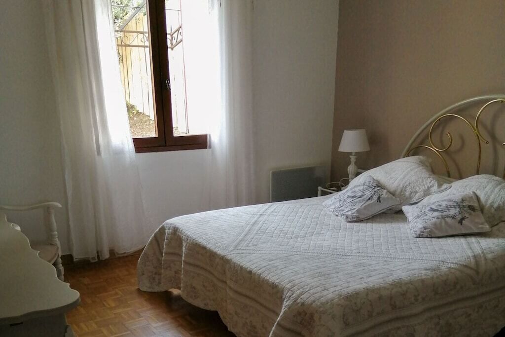 Een slaapkamer met een bed, nachtkastje, lamp en raam met gordijnen.